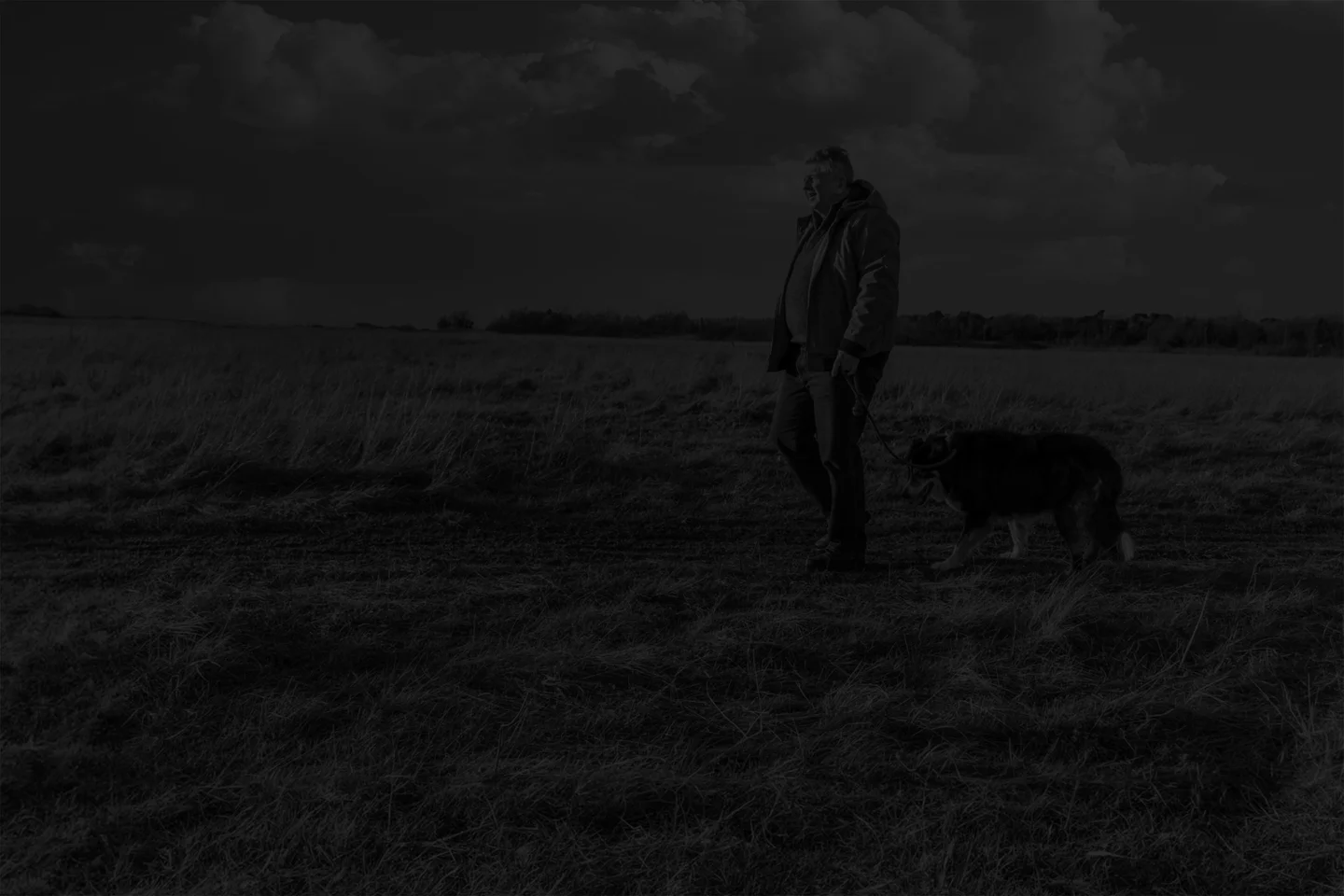 A man walking his dog in an open field on a sunny day
